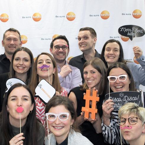 At Testo there is a unique team spirit Testo employees laugh happily into a photo box