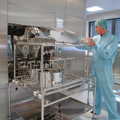 Person in cleanroom clothing inspects stainless steel equipment in a sterile production environment.