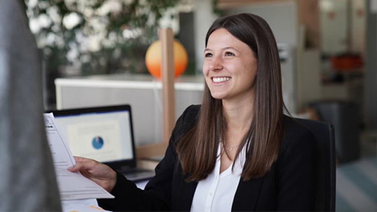 We bear responsibility - our values We bear responsibility - employee sits at desk and smiles at colleagues.
