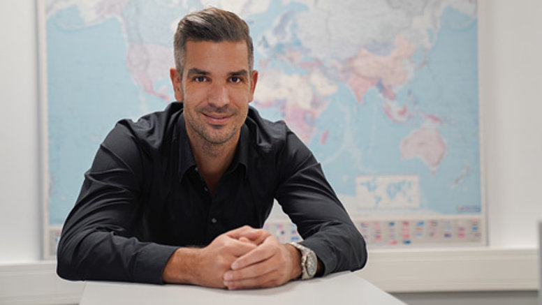 We are international - employee sits at desk and smiles, in the background is a world map.